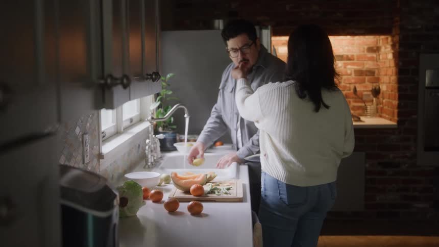A loving couple chops fruits and enjoys cooking together in the kitchen