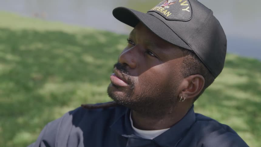 A man wearing a navy veteran cap looks up under sunlight