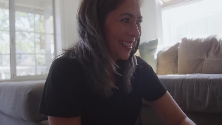 A woman sits crosslegged on a rug with a child sorting small square game pieces on the floor before looking up and smiling warmly as she shares a moment of playful interaction