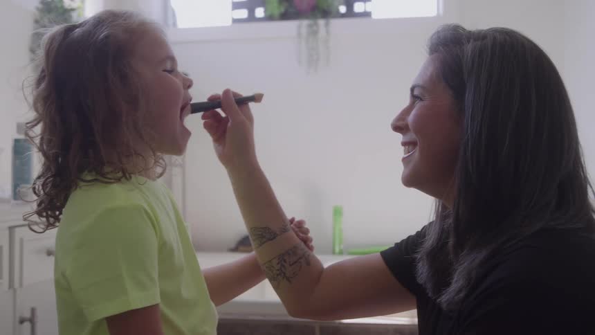 A mother is playfully putting makeup on her toddler daughter with a brush
