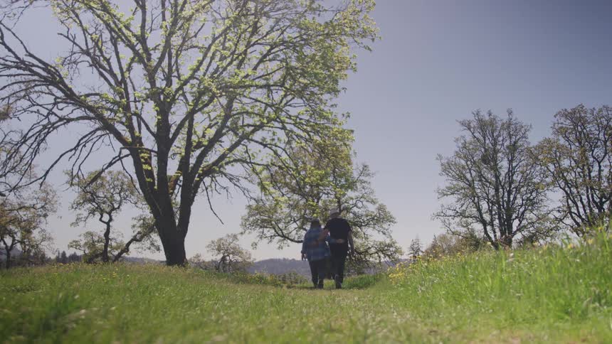 Two people hugging and walking on a grassy path at midday