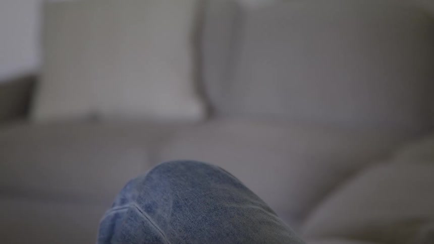 The video shows a closeup of a persons hand holding a remote controlthe person presses a button on the remote and then the hand moves out of the frame showing only the persons jeans and a sofa