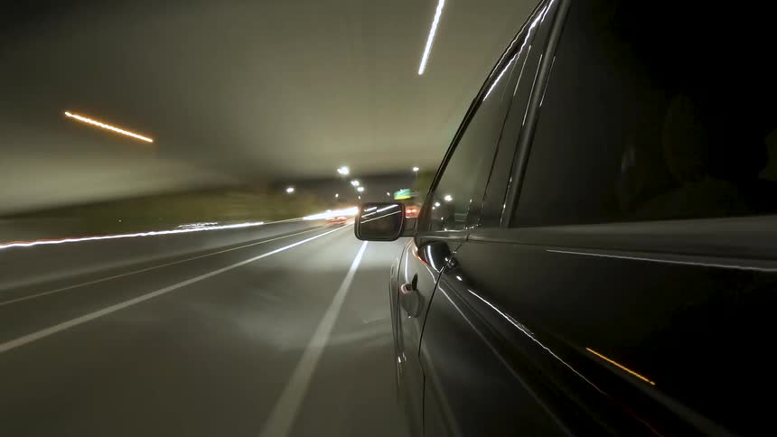 A black car drives along a city road at night