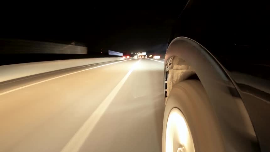 Black car driving on a road next to other cars wit an urban environment around outdoors during night time