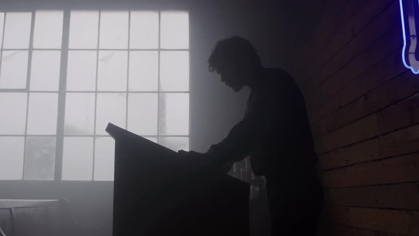Person standing at desk in dark room with lit window behind