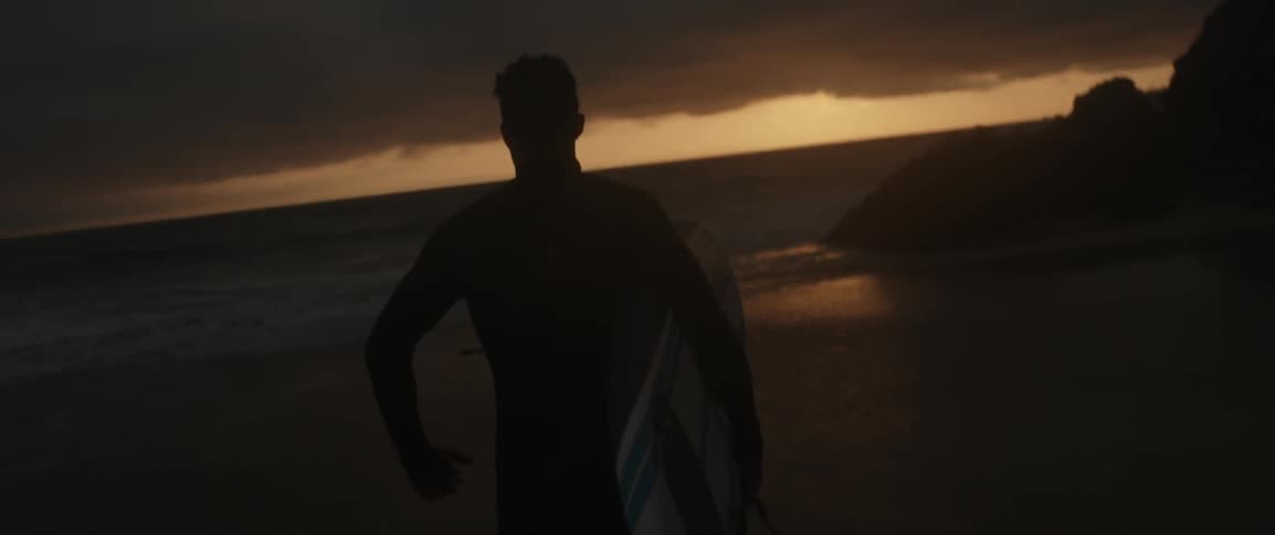 A man jogs along the shore holding a surfboard
