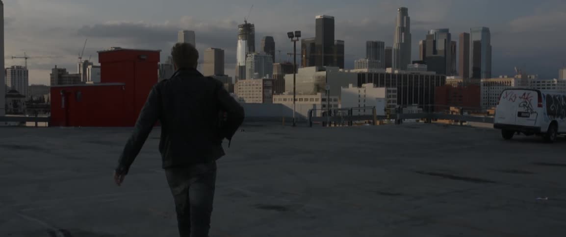 A man walks toward a car on a rooftop parking lot