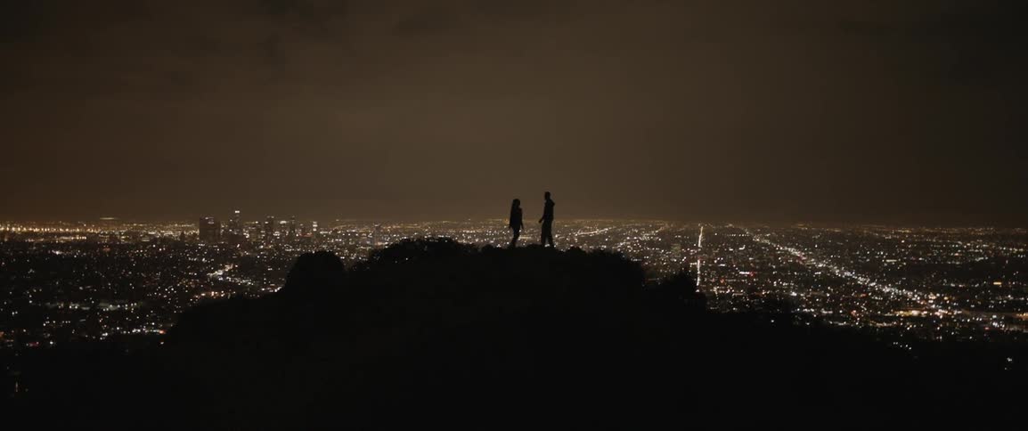 Two people on a hilltop overlooking a city at night