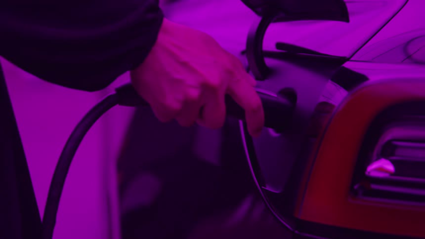 A male hand connects a charging dock to an electric car inside a garage preparing it to charge