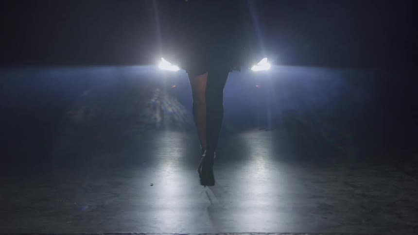 A model walks in front of a car in a dark environment illuminated by the glow of the cars headlights