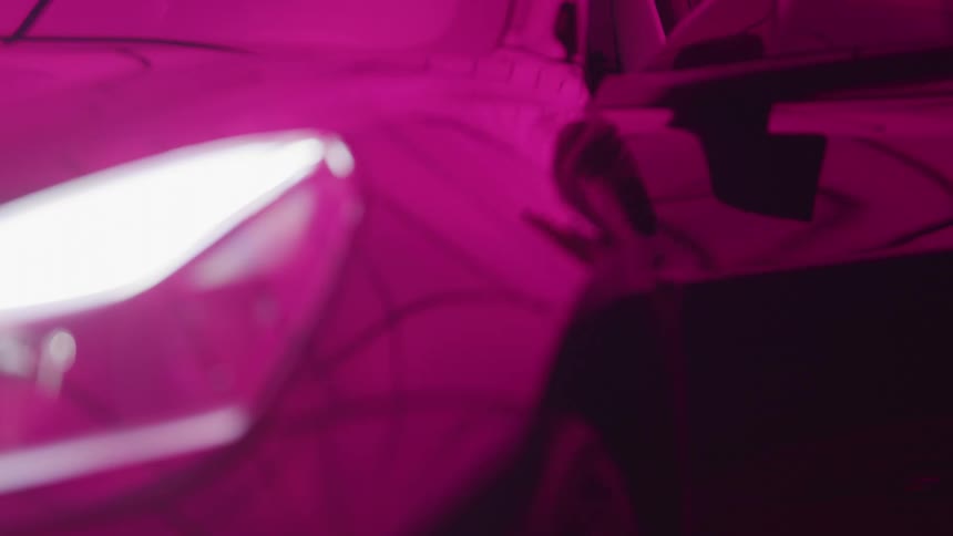 A persons hand reaches into the frame under bright pink studio lighting and pulls the handle to open the door of a dark glossy car