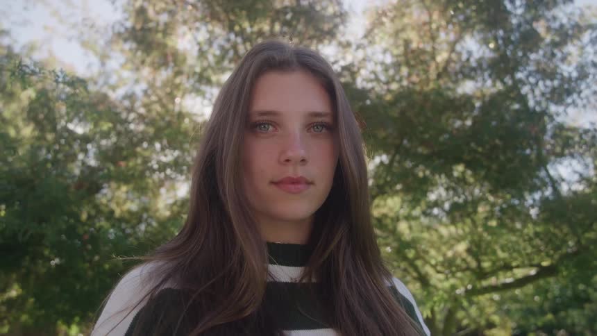 Teenager girl wearing a black and white sweater outdoors next to a grove during day time