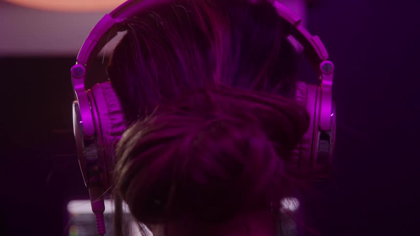 The head of a woman with her back turned with her hair tied up and wearing purple headphones