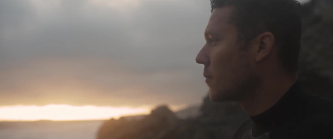 A man looks out at the ocean at sunset
