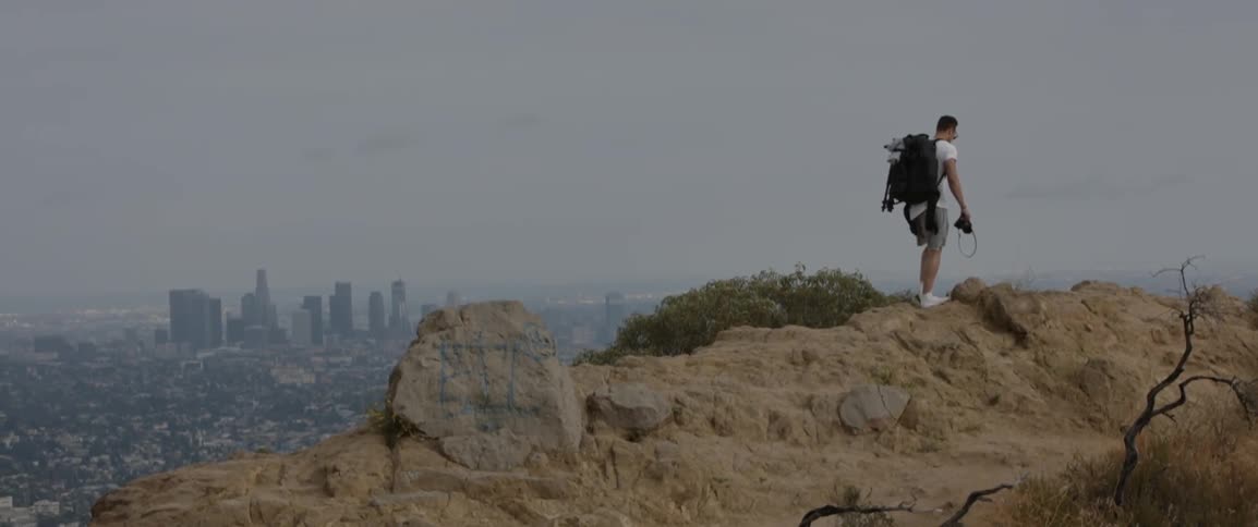 Man wearing backpack hiking up hill overlooking city