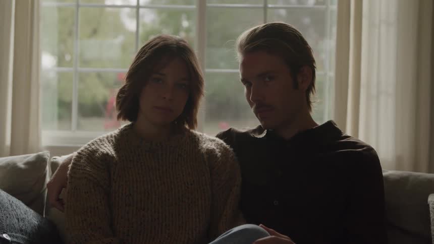 A young couple sits on a couch gazing into each others eyes indoors