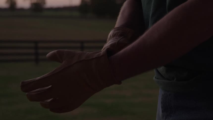 Person puts on work gloves in an outdoor area at dusk