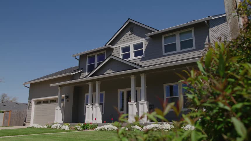 A modern two story home with a porch and landscaped lawn under a clear sky