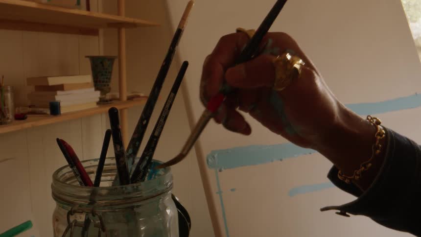 Closeup hand of a woman sticking the paint brush inside a glass jar
