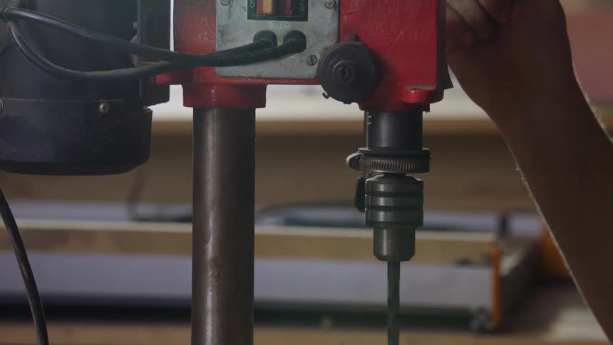 A close view of a person operating a red power drill press boring a hole into a block of wood on a workbench