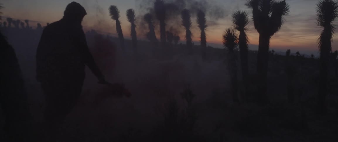 A man walks in the desert with a smoke can in his hand
