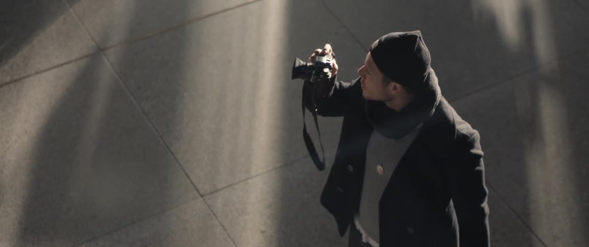 Man holding a camera and bag stands on a sidewalk