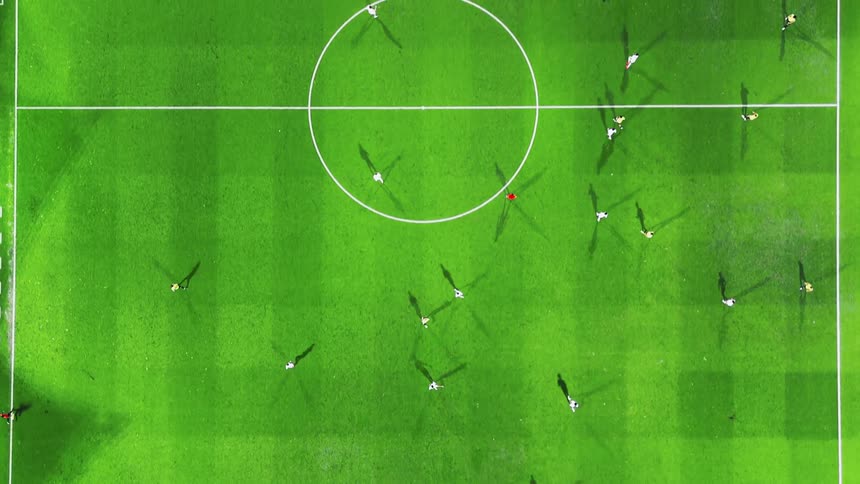 Soccer players playing on a sports field with a faint checkerboard pattern cast multiple shadows