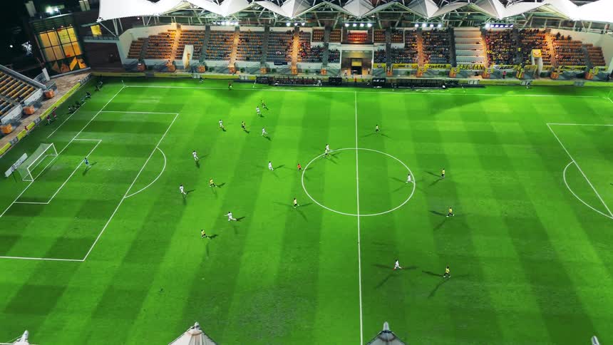 A highangle view tilts up from the green pitch to the stadium stands capturing a soccer match in progress under bright floodlights