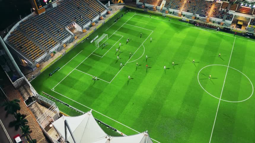 The video shows an aerial highangle view of a soccer football match taking place at night in a stadiumthe field is brightly lit and several players can be seen near one of the goals suggesting action near the penalty area