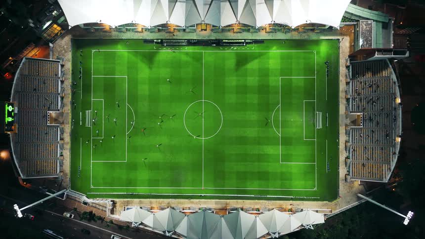 Illuminated stadium seen from above shows a match in progress on the field