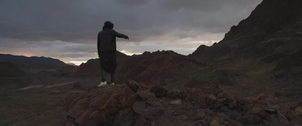 A man standing on a rocky mountain with many dark clouds in the sky