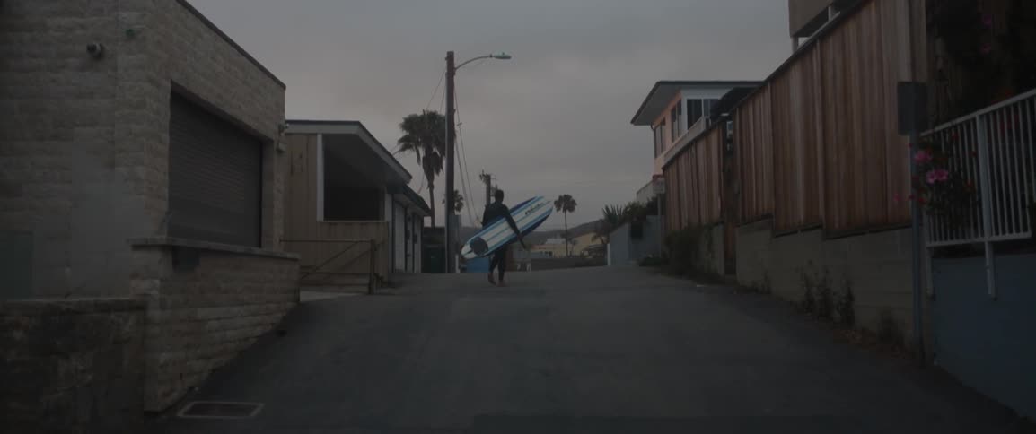 Person carrying a surfboard in an alleyway
