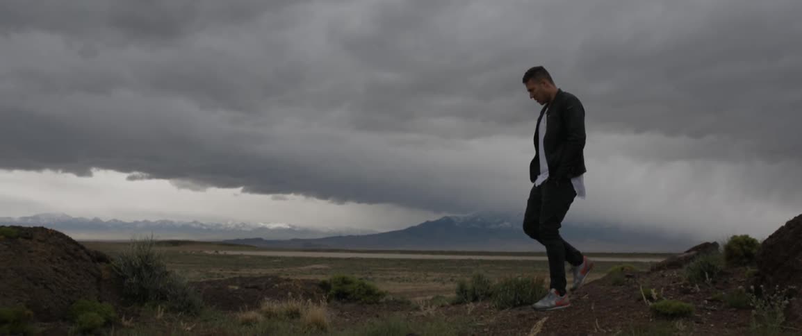 A man walks along a rocky ledge on a cloudy day