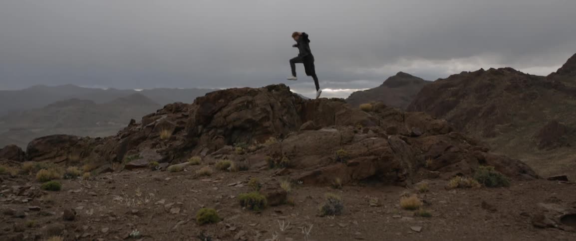 Man climbs up rocky hills on a cloudy day