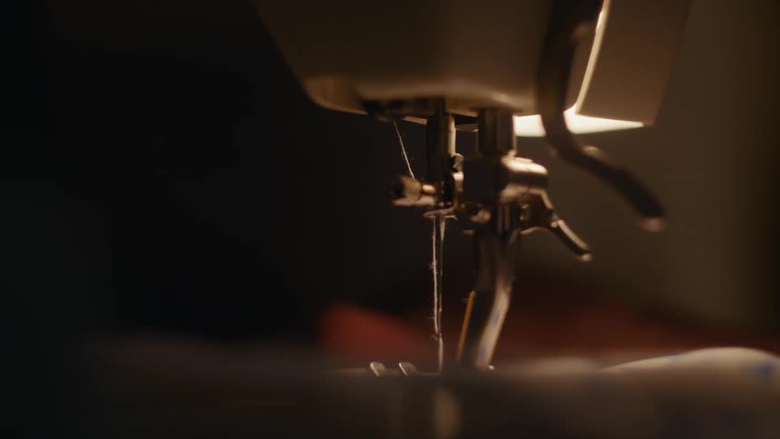 Person using a sewing machine guides fabric under the sewing needle