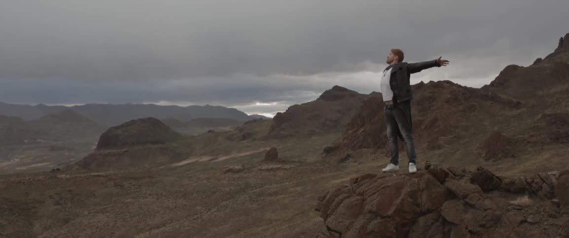 A man standing on a rocky ledge stretches his arms out