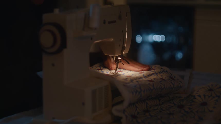Woman sewing on a patterned piece of fabric indoors during night time