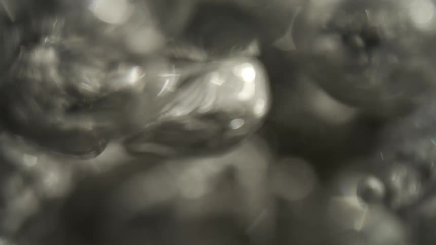 An extreme closeup handheld shot captures rapid streams of silver air bubbles rising through a dark liquid before shifting into an abstract blur