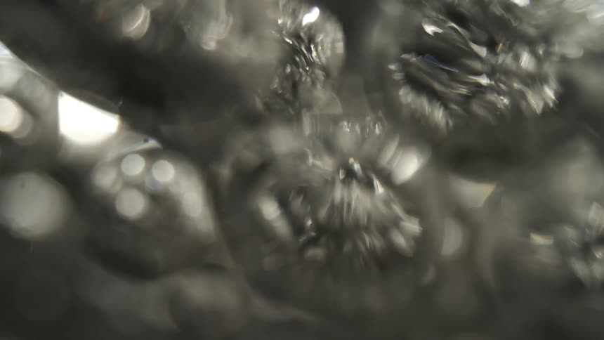 The video is an abstract closeup shot focused on shimmering and sparkling elements against a dark background possibly representing bubbles or faceted surfaces like diamonds or glassit shifts abruptly to a lighter heavily blurred section featuring