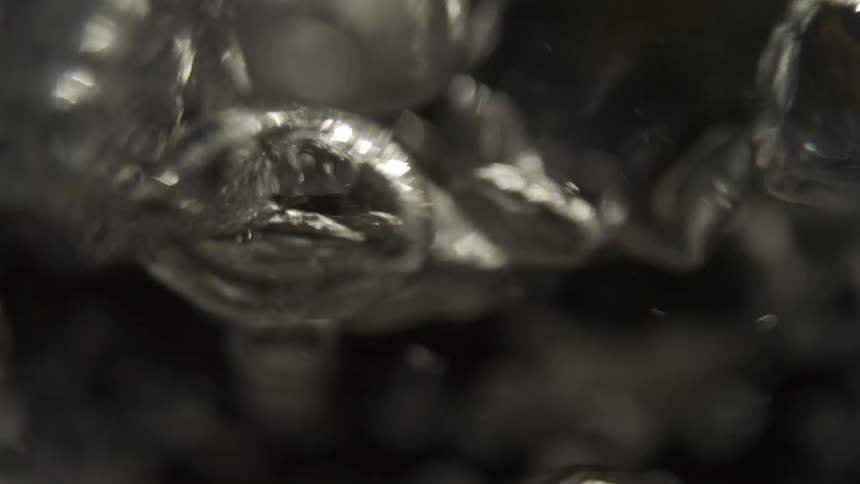 A close abstract view of numerous shimmering air bubbles rising and moving through dark water