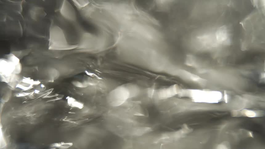 An abstract close view of water with blurred light reflections and bokeh highlights on a dark and metallic surface
