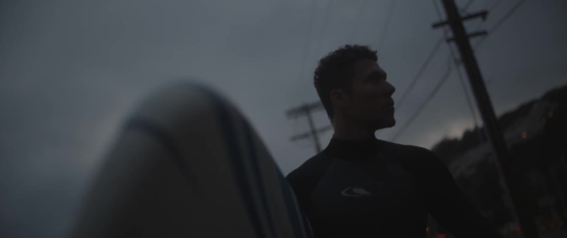 A man wearing a wetsuit carries a surfboard