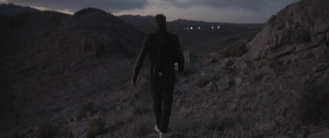 A man in a jacket walks on a rocky hill at night
