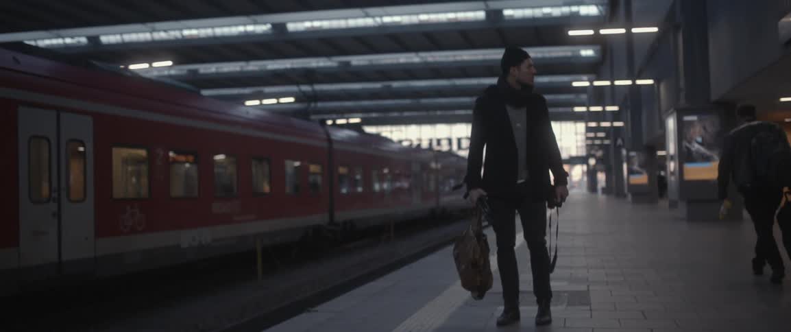 A man holding a bag and camera stands on a train platform