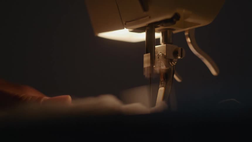 Needle stitching fabric guided by hand under focused light in sewing machine
