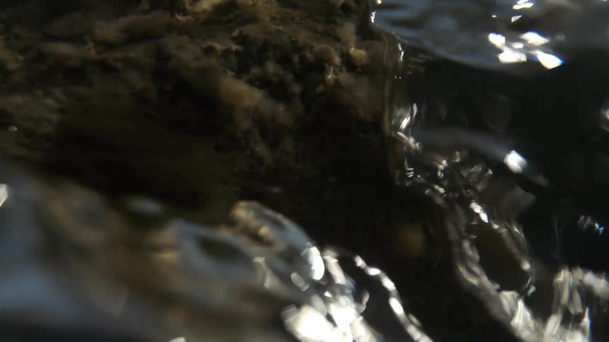 Flowing water surrounds submerged rock in continuous motion