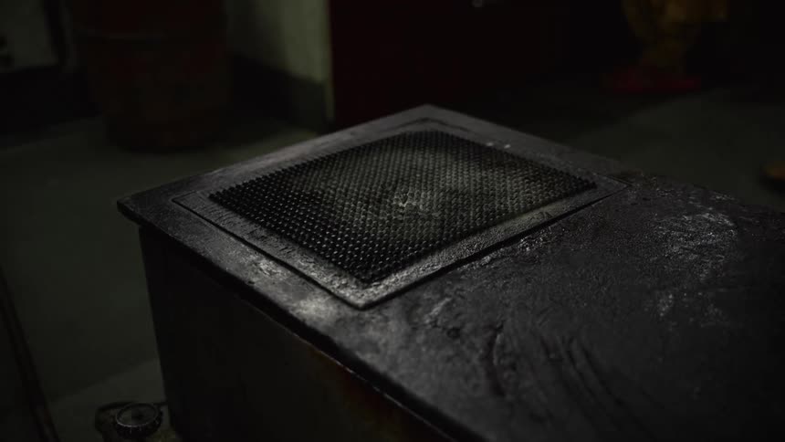 A hand quickly removes a wrinkled yellow cloth from a textured black metal surface in a dimly lit setting