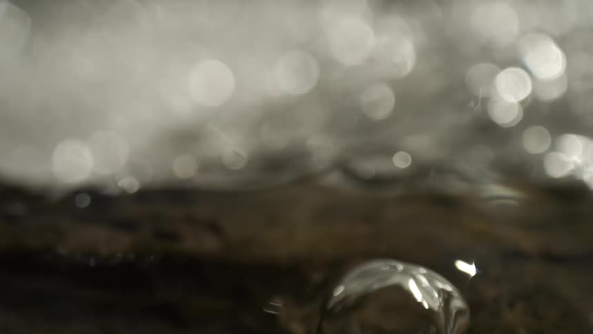 An abstract macro shot begins as a bright bokeh background and transitions to large clear bubbles floating in dark water