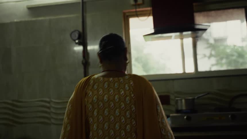Adult asian woman in a kitchen walking towards a stove where a pot is on the fire indoors during day time