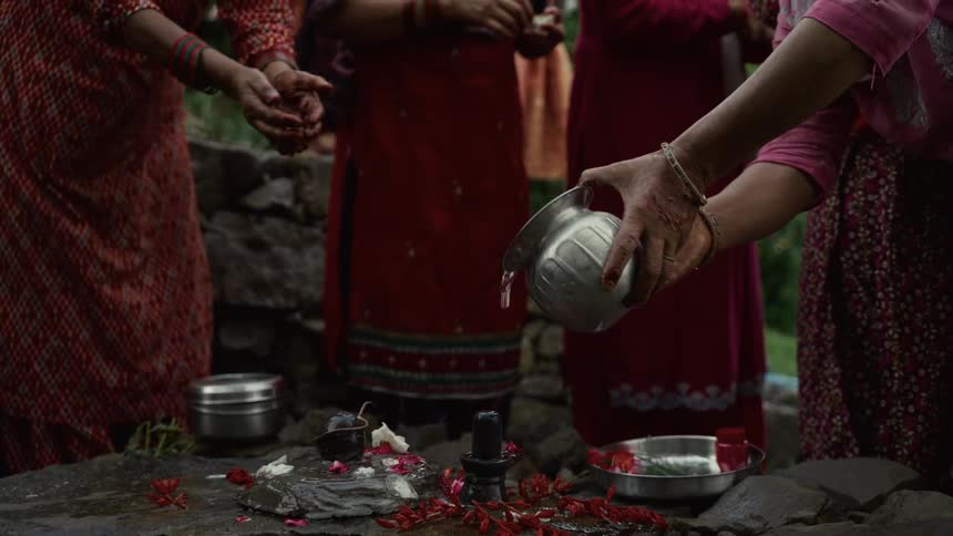Indian woman performs a ritual pouring water over a decorated shiva lingam outdoors
